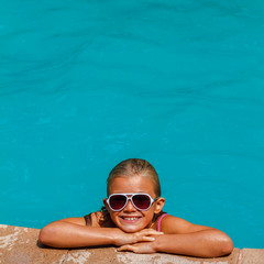 Pretty tanned and smiling girl in sunglasses swimming in the swimming pool at the resort in vacation