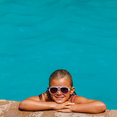 Pretty tanned and smiling girl in sunglasses swimming in the swimming pool at the resort in vacation