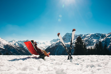 guy chilling out on the slope after skiing in Aprica ski resort with his skies next to him - obrazy, fototapety, plakaty