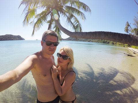 Young couple sunbathing in a sea near palm at wild beach at summer vacation