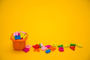  Many multicolored wooden letters on a yellow background. toy letters. letters in an orange bucket. english alphabet. design concept. View from above. Flat lay. Copy space for text.
