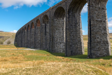 Fototapeta na wymiar The sweeping majestic Ribblehead Viaduct stands tall above the Ribble Valley, Yorkshire, England carrying the Settle to Carlise railway against a bright blue sky