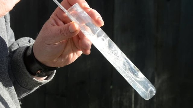 A person outside the frame blows air trough a solution of calcium hydroxide (lime water) The CO2 of the exhalation causes a reaction where solid chalk causes the liquid to become white and blurry. 