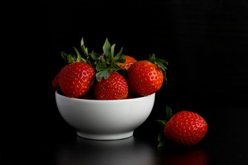 fresh strawberries in a bowl on black background