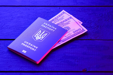 Ukrainian biometric passport and dollars. Ukrainian international passport on black boards, top view. Document for traveling abroad in blue light