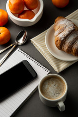 Delicious breakfast coffee with croissant and citrus fruits. Heart shaped box. Work table with smart phone. French pastry and cup of coffee. Template for social media. Copy space.