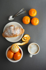Delicious breakfast coffee with croissant and citrus fruits - oranges. Morning caffeine. French, fresh pastry and cup of coffee or latte. Caffeine adicted.