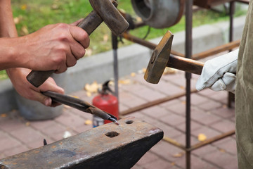 Work with hammers on the anvil in the street forge workshop.