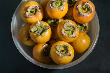 Washed wet persimmons in a bowl on the table, close up