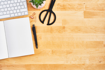 Wood office desk table with blank notebook, pen, computer, plant and scissors. Top view. Copy space for text. Flat lay.