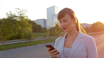 LENS FLARE: Businesswoman looking at her cell phone while walking down sidewalk