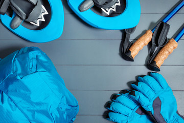 Flat lay top view on winter hiking and snowshoeing equipment with blue backpack and gloves with trekking sticks