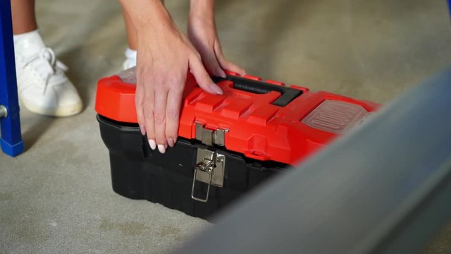 Woman worker opens toolbox and takes hammer.