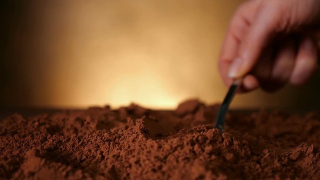 Hand with spoon pushing through cocoa powder lifting up a dose - close up, slow motion, static camera