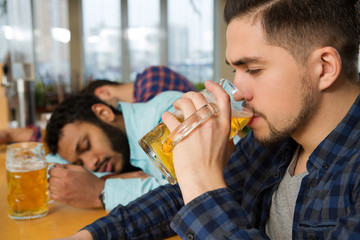 Still standing. Cropped shot of a young bearded man drinking beer as his friends sleeping on the table