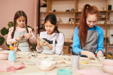 Multi-ethnic group of schoolchildren making handmade ceramics in pottery class - obrazy, fototapety, plakaty