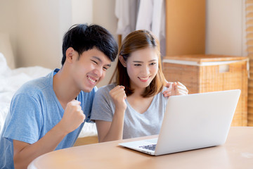 Beautiful portrait young asian couple working laptop with smile and happy sitting in bedroom, man and woman using notebook computer with excited and satisfied, business and success concept.