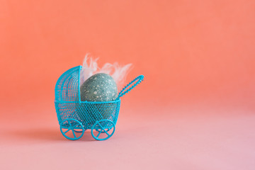 Blue Easter egg in a blue baby carriage on a red coral background