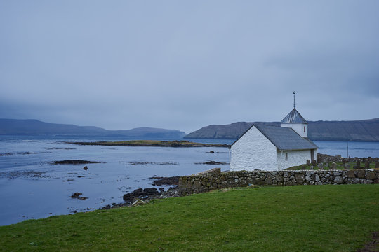 Saint Olav's church on the bank of deep fjord in atlantic ocean in village Kirkjubour on the island Streymoy in Faroe islands. Picture taken in rain and windy scandinavian weather condition in spring.