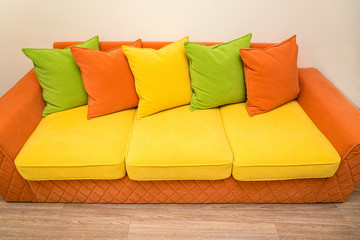 a colorful yellow-orange sofa with green, yellow and orange pillows