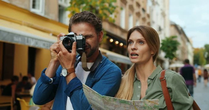 Caucasian beautiful woman and handsome man strolling the city as tourists with a map and photocamera while man taking photos.