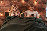 Couple addicted to social media lying in bed and using smartphones