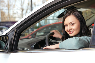 Fototapeta na wymiar Woman on the road. Portrait of a beautiful happy brunette smiling to the camera sitting in a new car at the car salon
