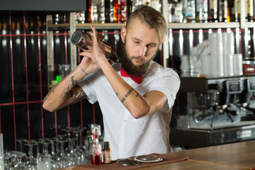 Stunning. Horizontal shot of hardcore tattooed bartender attentively mixing drinks.