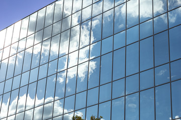 The side of the a glass encased building reflecting bright clouds on a sunny day