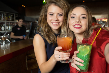 Time for selfie. Two seductive smiling and charming female drinking at the restaurant.