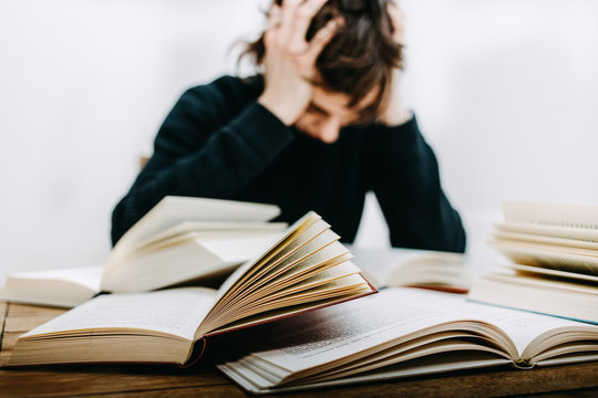 Student sitzt verzweifelt am Schreibtisch vor im einige aufgeschlagene B&uuml;cher 
