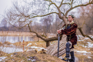 Costume Play Art Photography. Lonely Knight In Medieval Outfit Posing in Forest Outdoors Against...