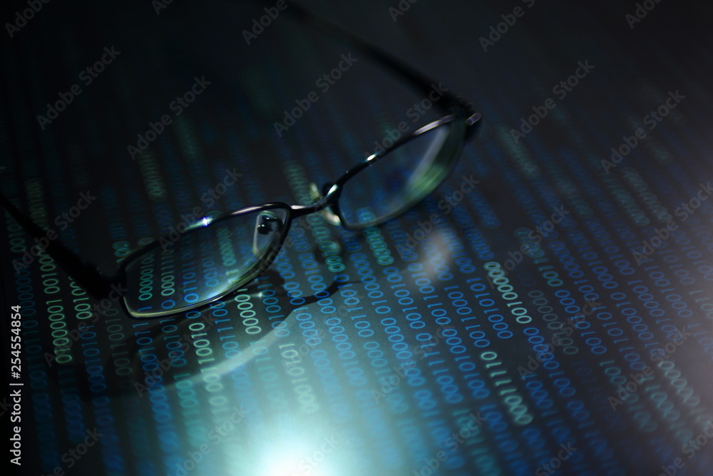 Poster reading data in digital age. glasses and flowing binary code matrix. shallow depth of field image of glasses on display panel. multiple lines of blue code moving under glasses.