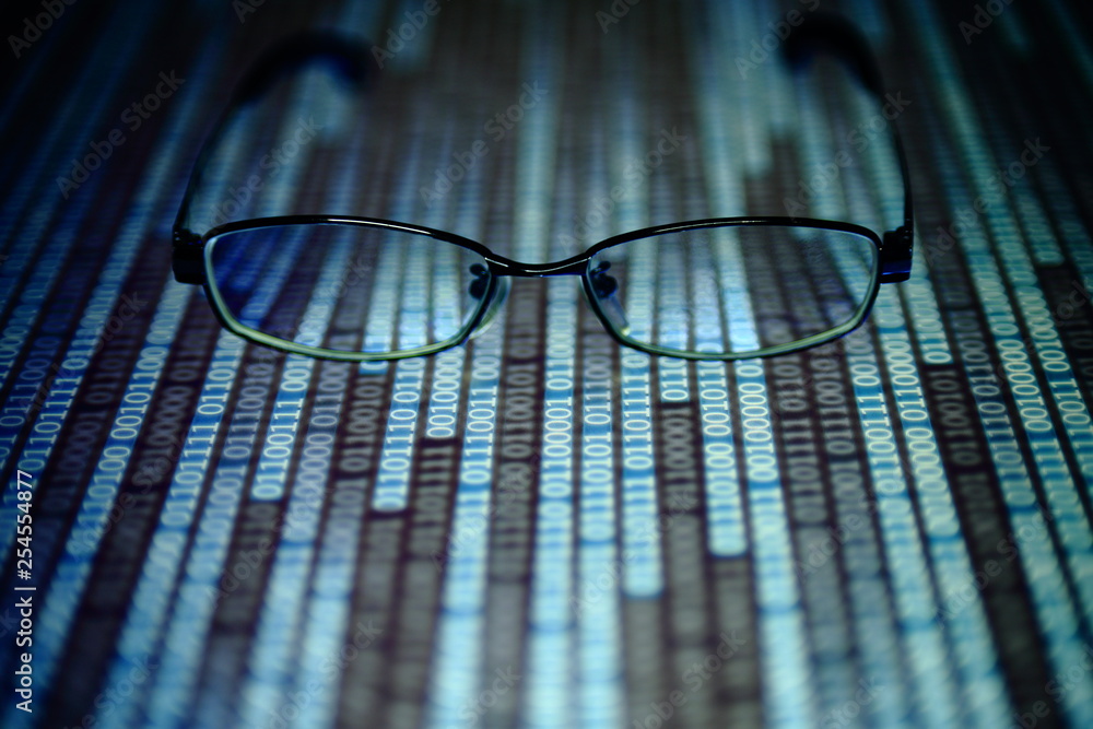 Aufkleber reading data in digital age. glasses and flowing binary code matrix. shallow depth of field image of glasses on display panel. multiple lines of blue code moving under glasses.