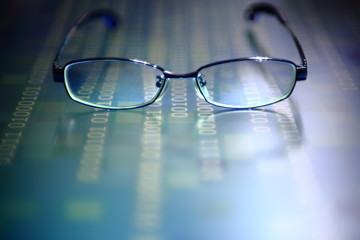 big data analysis. glasses placed on a LED digital panel display white light one and zero binary text number in moving motion pattern. modern technology blue block grid pattern backgrounds