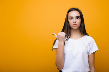 Beautiful young woman with long hair and dressed in white looking surprised at camera and pointing...