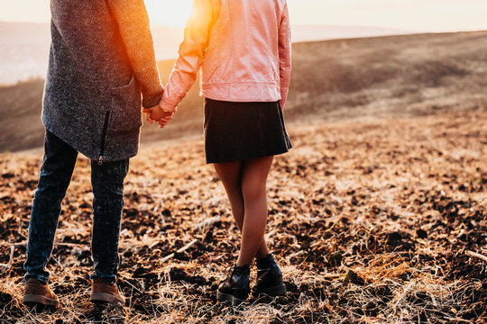 Crop view of couple legs and holding hand against sunset while dating outside .