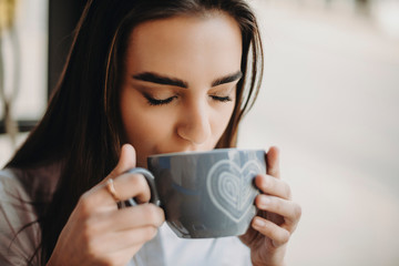 Lovely young woman student drinking a cup of coffee after lessons in a caffe . Close up of a beautiful woman drinking coffee.