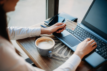 Side view of female hands holding a plastic gold credit card and using a laptop while sitting in a coffee shop . Online banking concept. Online shopping concept.
