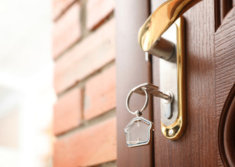 Key with house-shaped trinket in door lock, closeup. Space for text