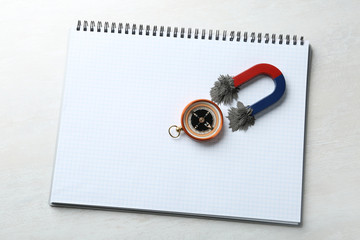 Notebook, compass and magnet with iron powder on light background, top view. Space for text