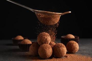 Tasty chocolate truffles powdered with cocoa from sieve on grey table