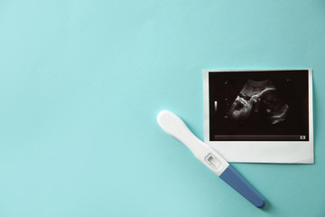 Ultrasound picture of baby and pregnancy test on color background, top view with space for text