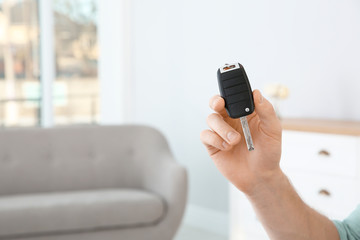 Young man with new car key in dealership, closeup. Space for text