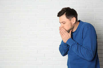 Man suffering from cough near brick wall. Space for text