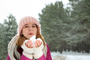 Beautiful woman blowing snow in winter forest. Space for text