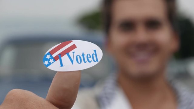 Young man lifts up a generic "I Voted" sticker in the frame.