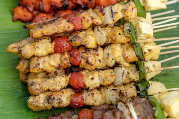 Skewers with pieces of grilled barbecue, green bell pepper, red tomato and meat for sell in street market, Thailand, closeup