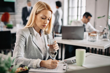 Businesswoman witting notes while going through business reports at work.