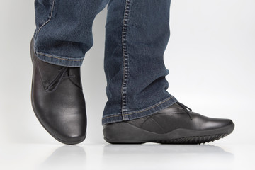Men's legs in jeans and black classic shoes on white background
